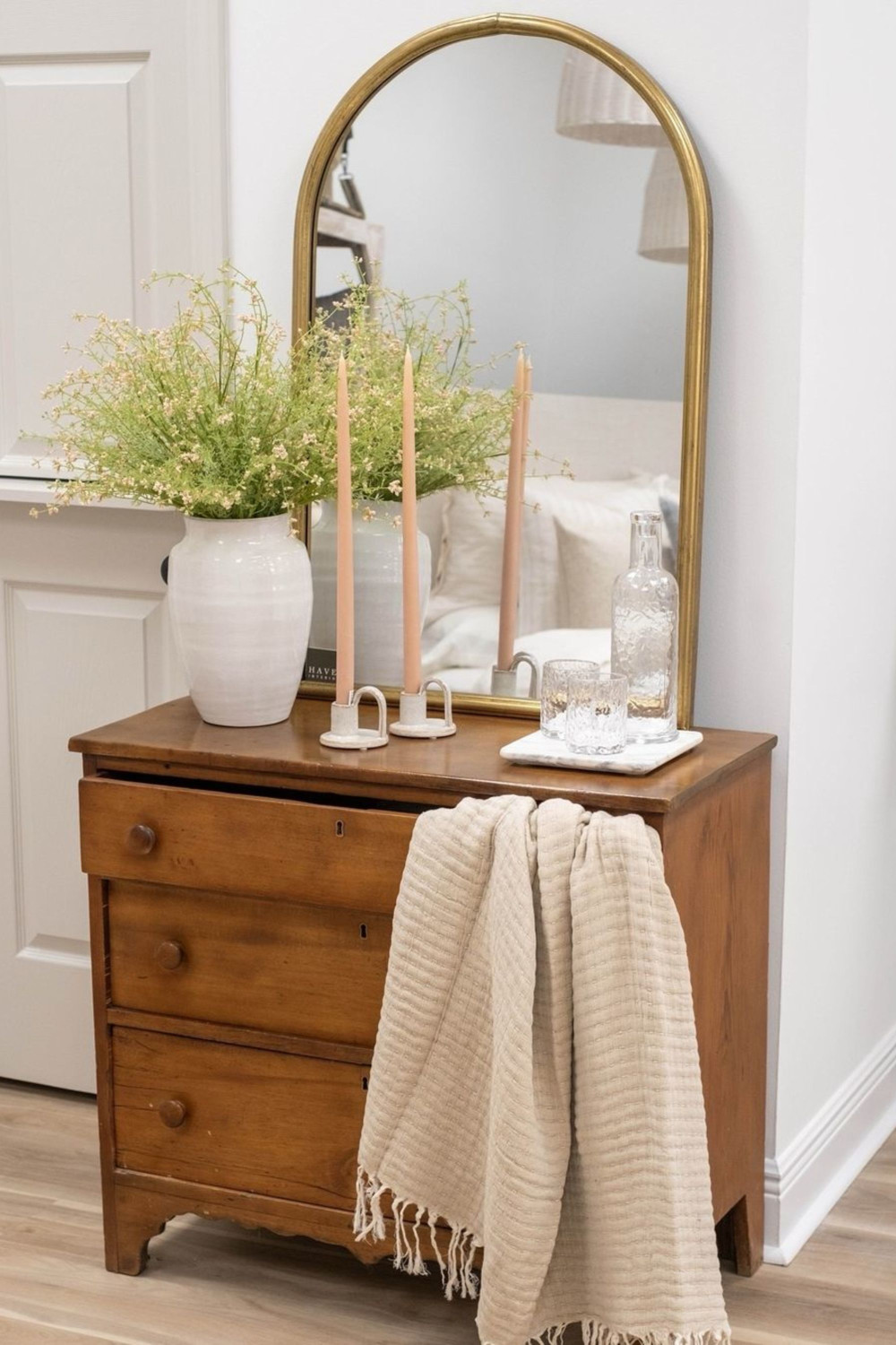 arched mirror over chest of drawers with styling in bedroom